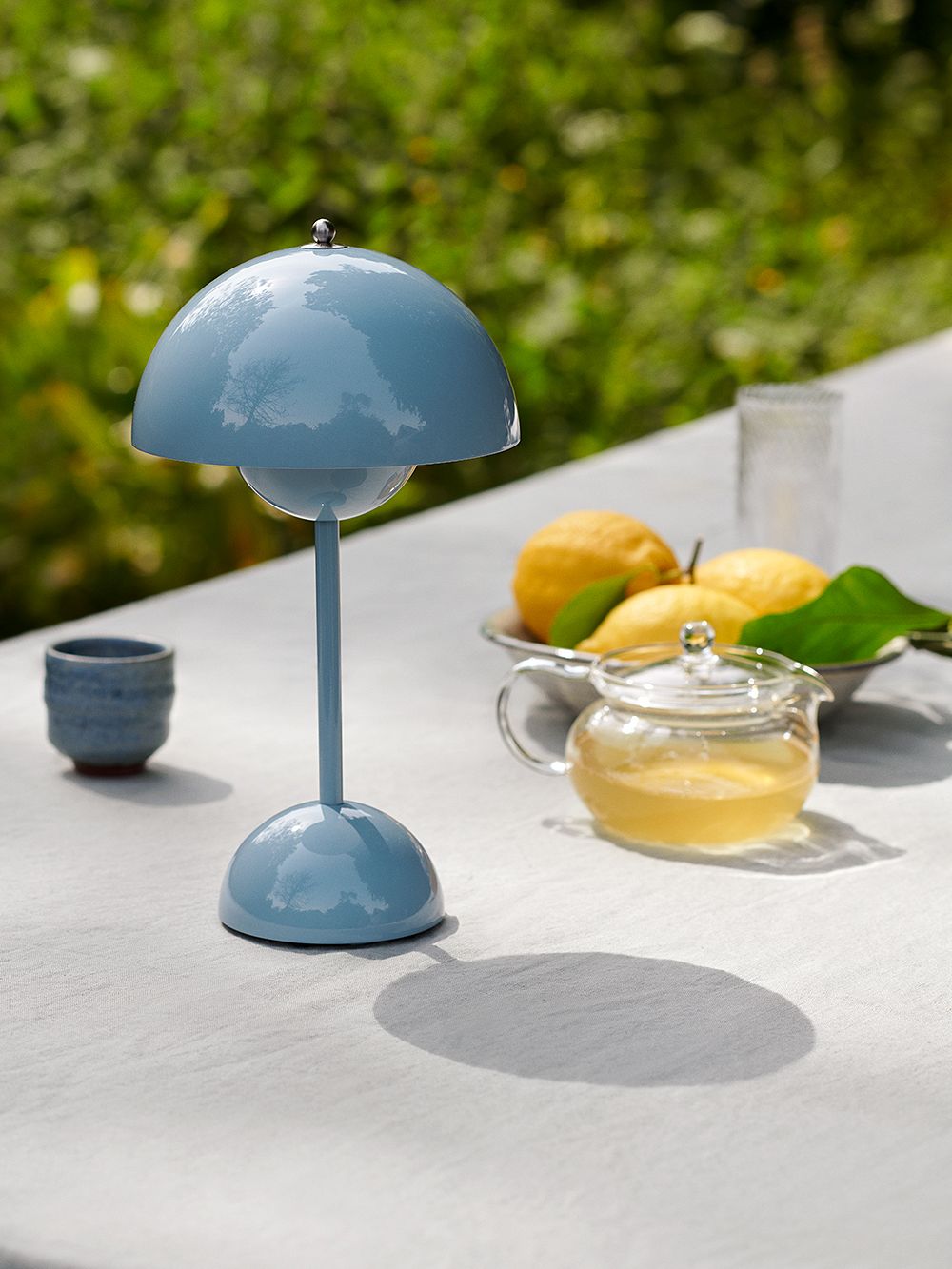 Kuva, jossa &Traditionin kannettava Flowerpot VP9 -pöytävalaisin vaaleansinisessa sävyssä pöydällä, osana kesäkattausta.